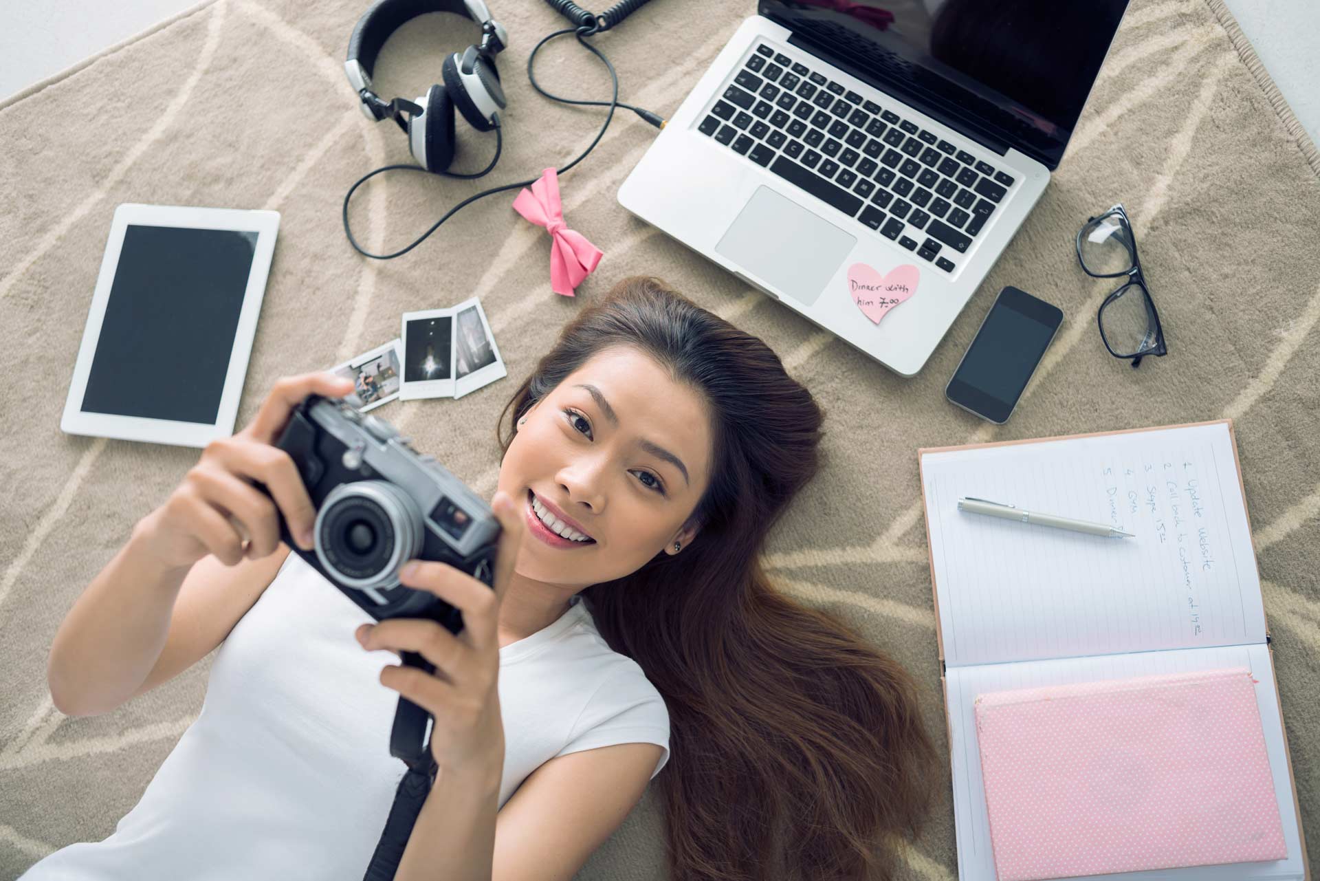 Cheerful Vietnamese girl lying on the floor with her camera in hands